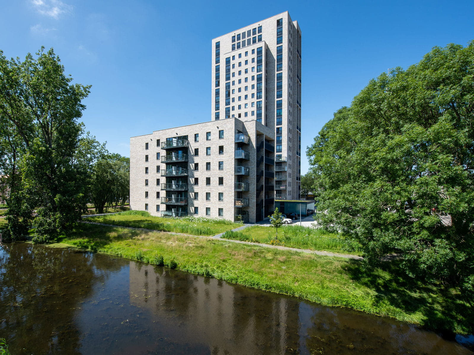 gebouw met lichte gevelstenen en steenstrips met water en groen op de voorgrond