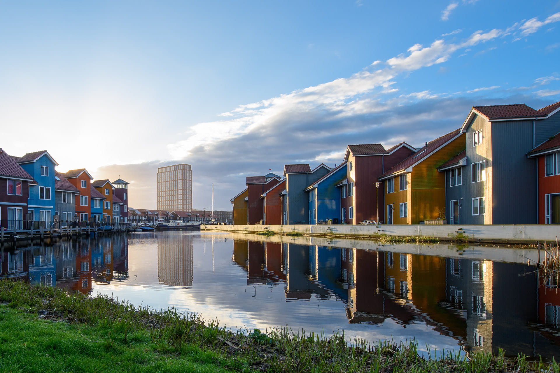 Een water met huizen op de voorgrond en een toren in de verte