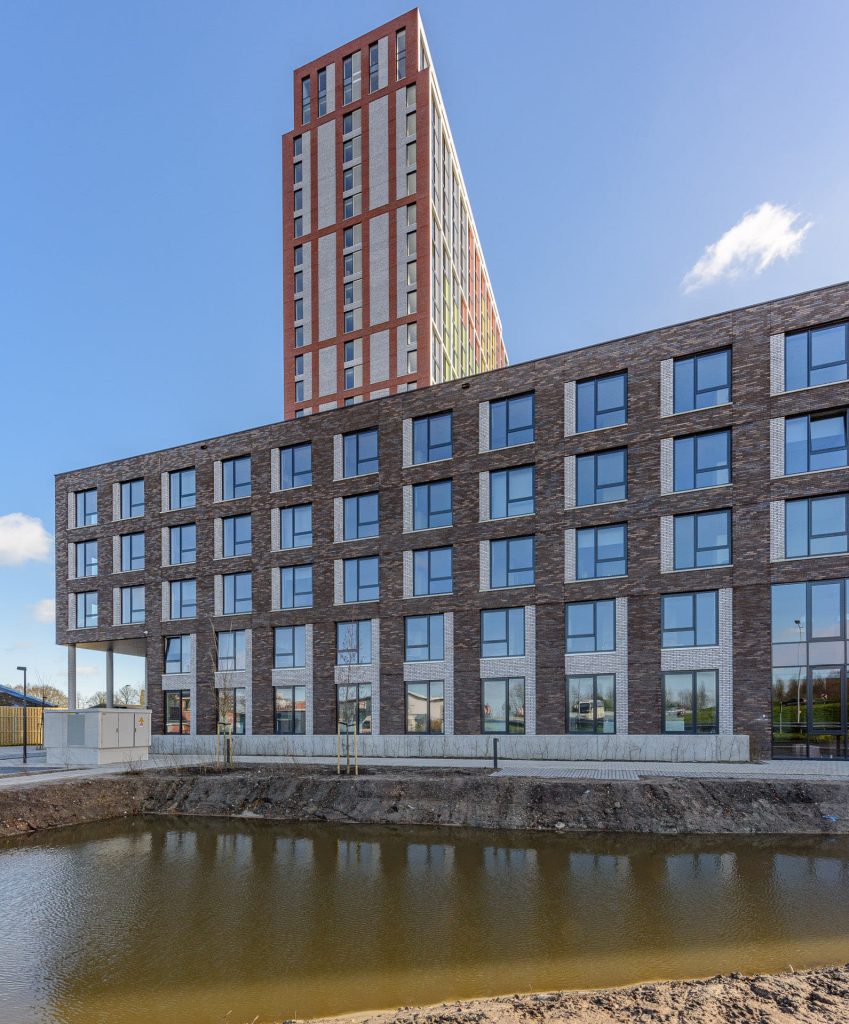 Gebouw met bruinige steen en ervoor water, met erachter de toren die tegen een blauwe lucht afsteekt