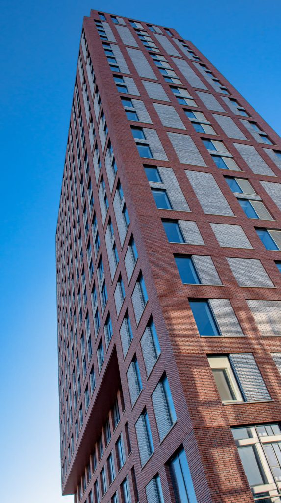 Zijkant van een toren met rode gevelstenen en lichte vlakken tegen een blauwe lucht