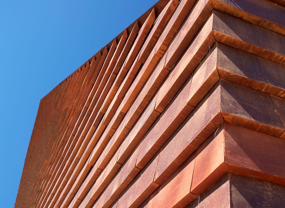 Detail van een rode muur met grote rode sidings tegen een blauwe luchtDetail van een rode muur met grote rode sidings tegen een blauwe lucht