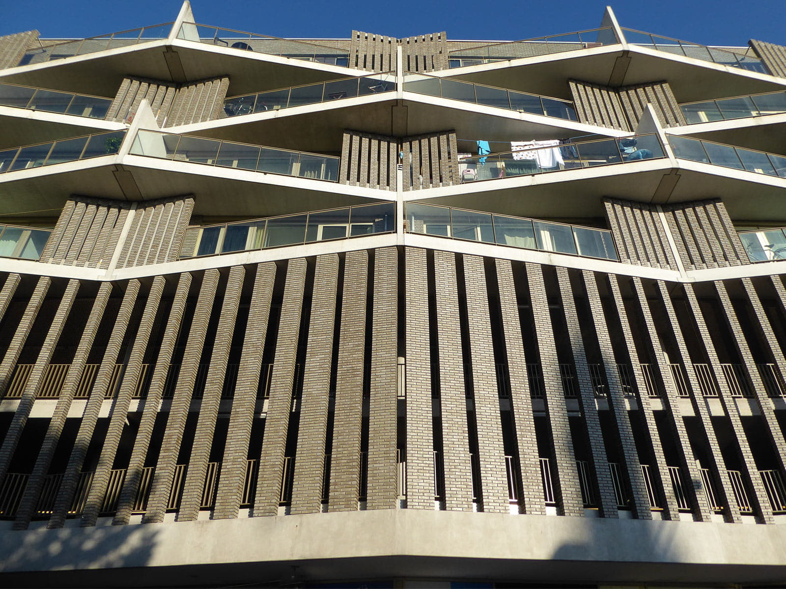 Zicht van onderen op een bruine gevel van een hoog gebouw met schuine lijnen en ramen