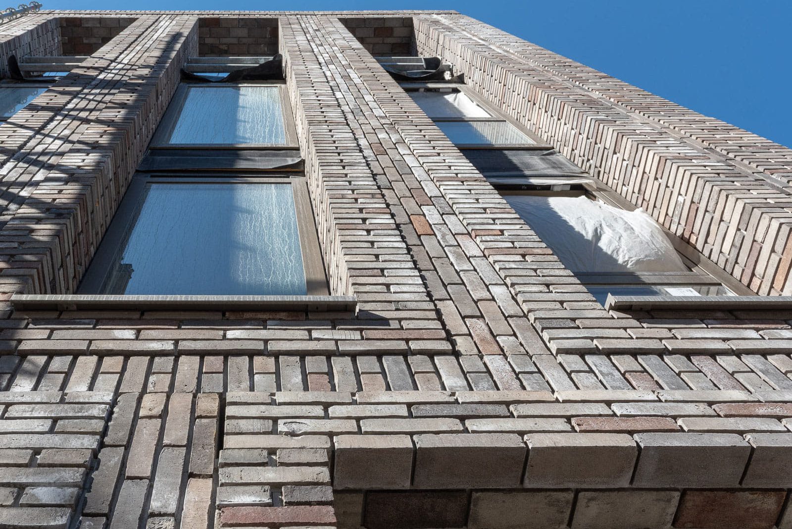 Een gebouw van onderen gezien, met uitsteken metselwerk en terugliggende stenen in lichte kleur